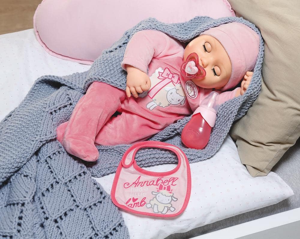 Baby Annabell doll sleeping peacefully on a bed, covered with a blanket, with her pacifier in her mouth and bottle nearby.