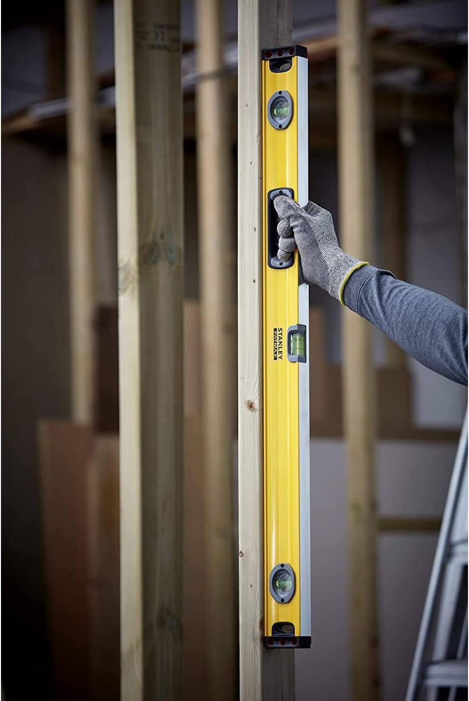 A person using the Stanley FatMax Level to check the vertical alignment of a wooden stud from a different angle.