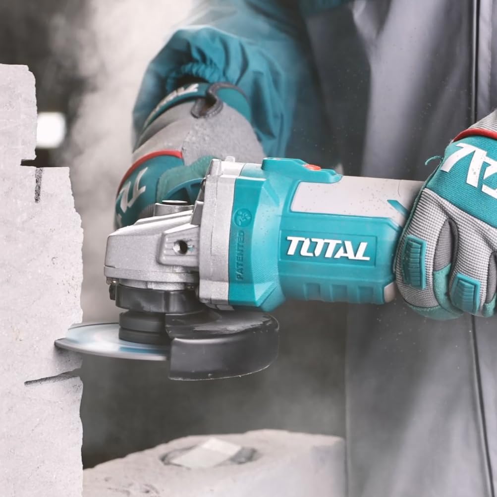 User operating the TOTAL P20S 20V Cordless Brushless Angle Grinder to cut a stone block, generating dust.