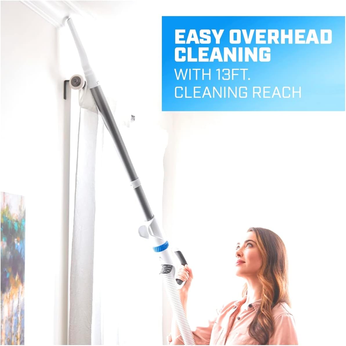 Woman using the crevice tool of the HART Pro Upright Vacuum to clean high corners and ceiling edges, demonstrating the 13-foot cleaning reach.