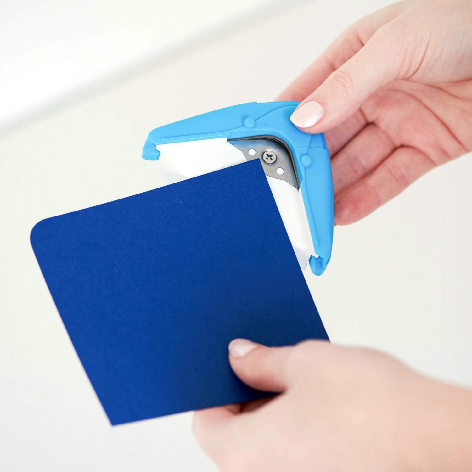 Hands using the corner rounder on blue paper to create a rounded corner