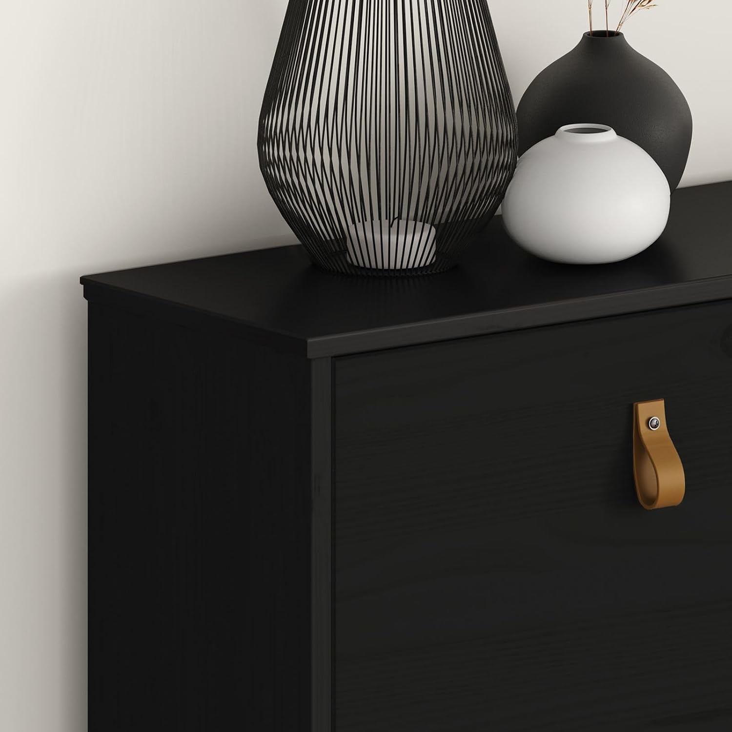 Close-up of the top surface and a leather handle of the black IDIMEX MIKKA Shoe Cabinet, showing the lacquered finish and natural wood grain.