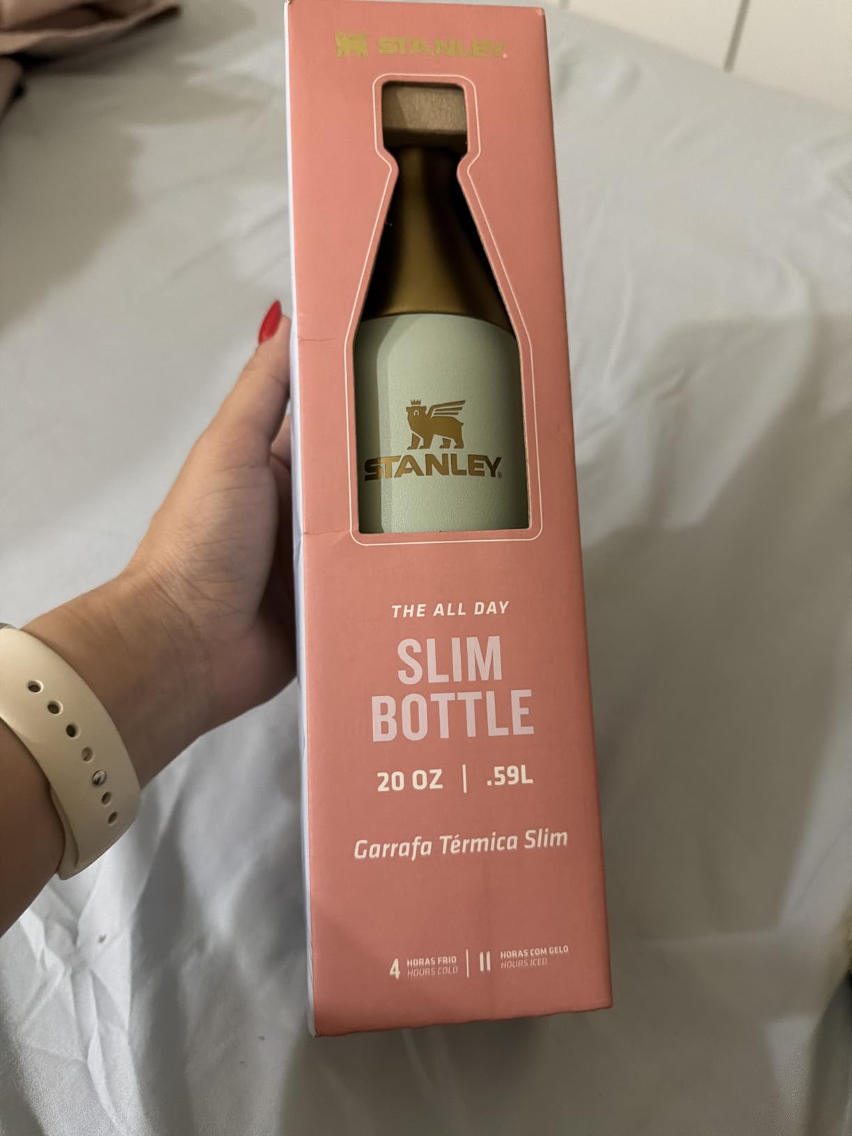Mão segurando a caixa da garrafa térmica Stanley Slim Bottle 591ml com a embalagem original visível