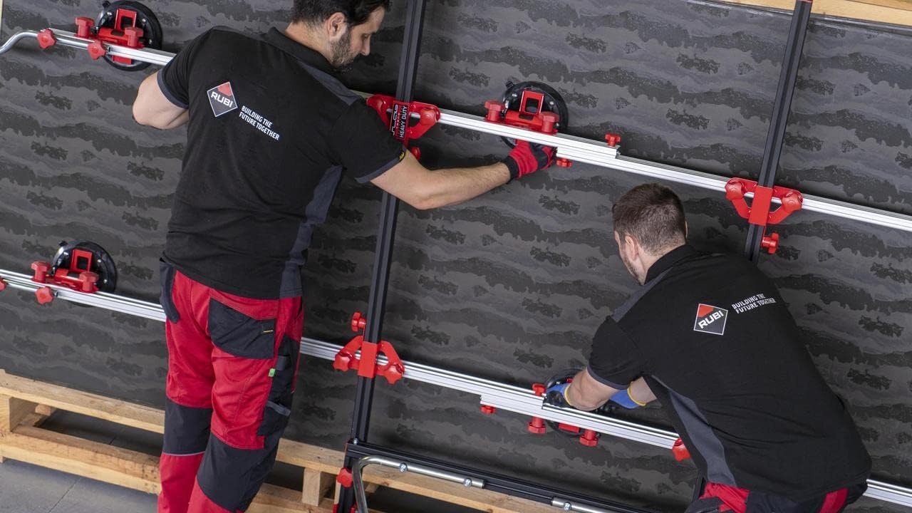 Two workers adjusting a large dark-colored slab vertically, with the RUBI Slim Easy Trans Plus attached, showing precise positioning.