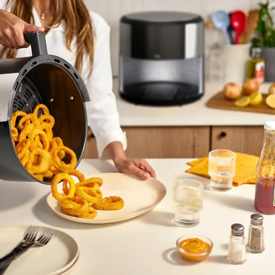 Person pouring crispy onion rings from air fryer basket onto a plate