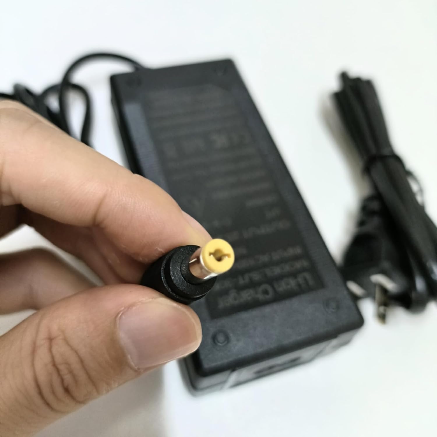Hand holding the barrel connector of the charger, ready to plug in