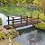 7' Wooden Garden Bridge with Safety Rails, Backyard Footbridge for Ponds, Creeks, and Streams, Stained Finish, 396 lbs Capacity