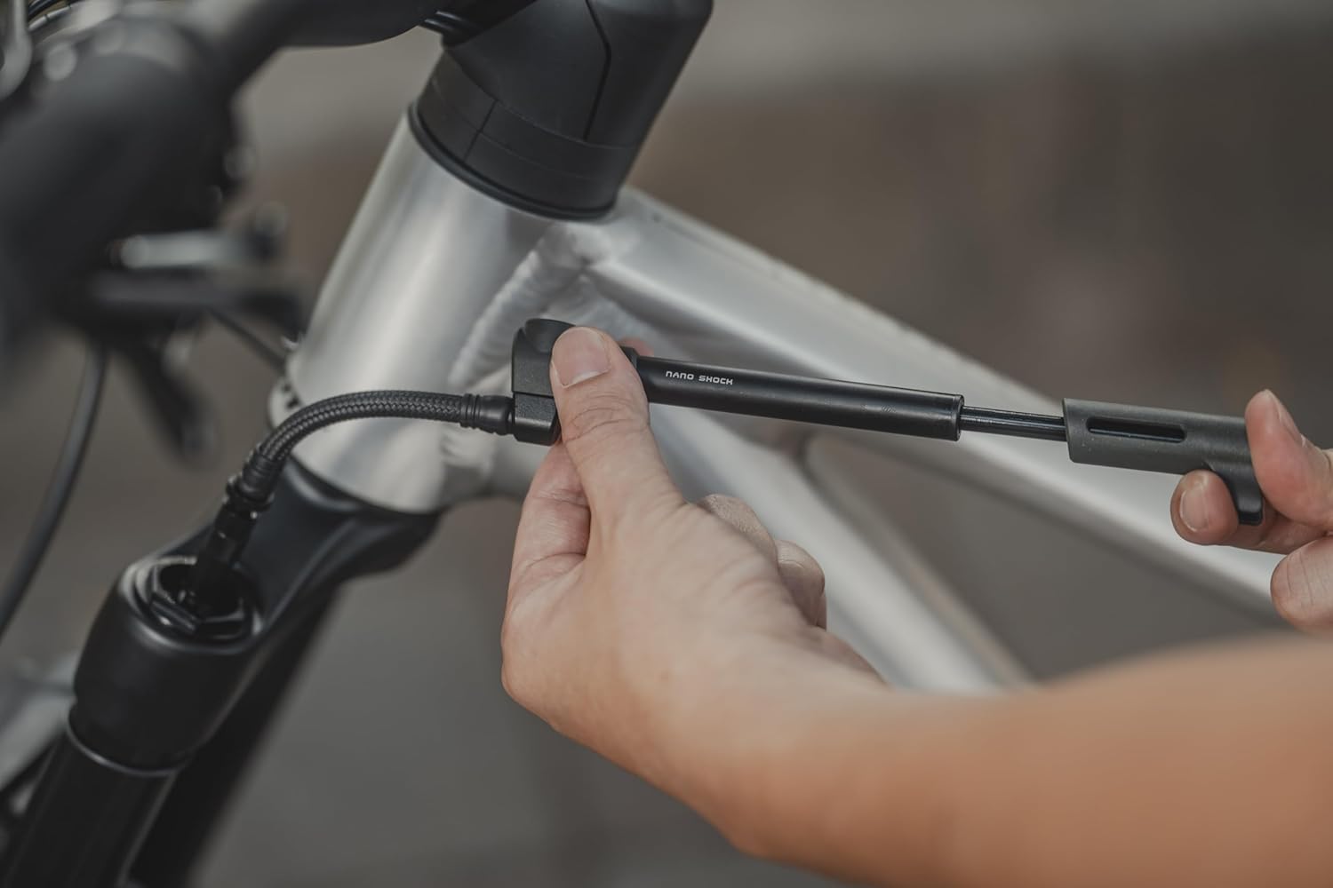 A person connecting the Topeak Nano Shock Pump to a bicycle's suspension fork.