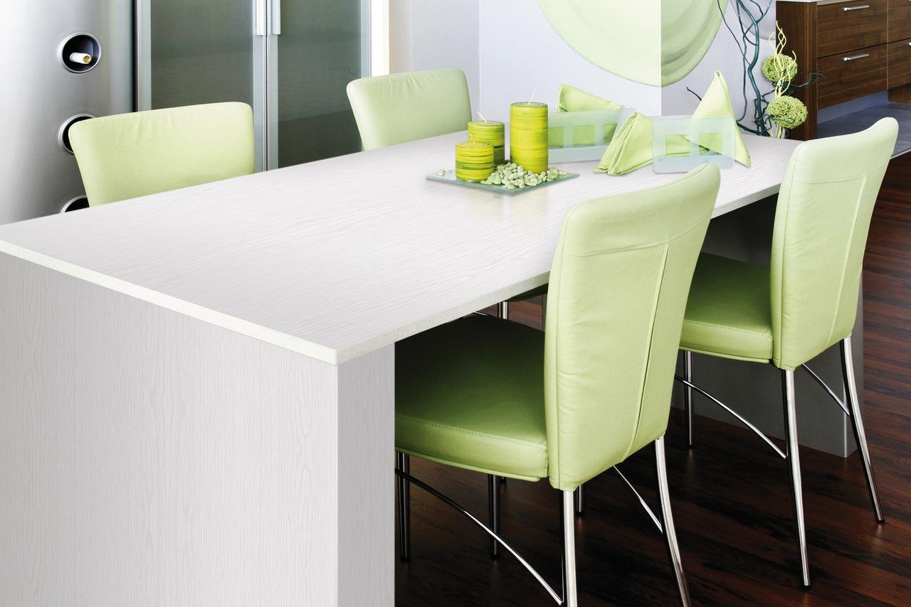 Dining table with a white wood grain top, covered with d-c-fix Whitewood film, surrounded by green chairs.