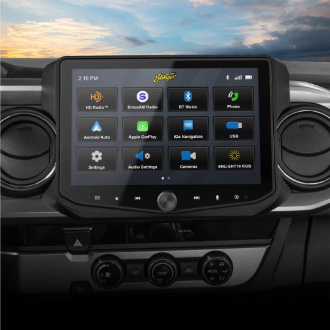 Detailní záběr view of the Stinger HORIZON10/HEIGH10 infotainment system installed in a Toyota Tacoma dashboard, displaying its main menu with icons for HD Radio, SiriusXM, Bluetooth, Phone, Android Auto, Apple CarPlay, Navigation, USB, Settings, Audio Settings, Cameras, and ENLIGHT16 RGB.