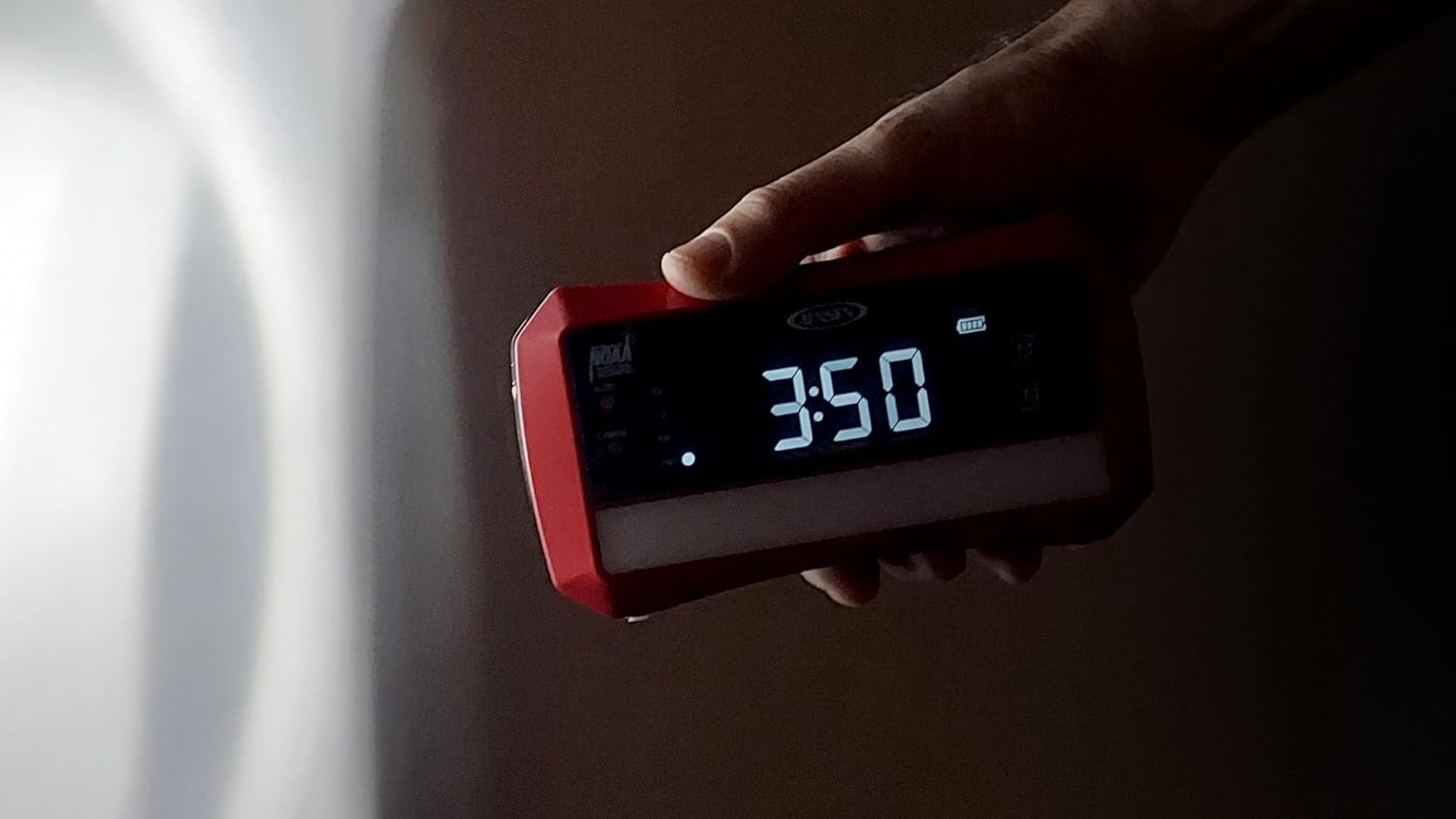 A hand holding the Jensen JEP-775 radio with its side flashlight illuminated, casting a beam of light