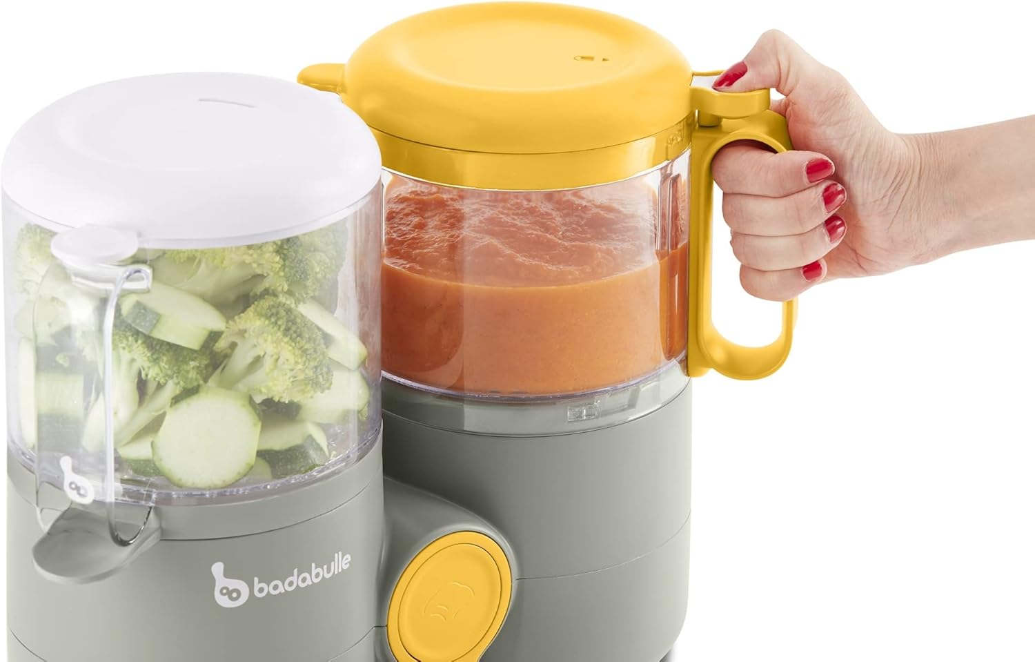 A hand holding the blending jug of the Badabulle B-Easy food processor, showing blended food inside.