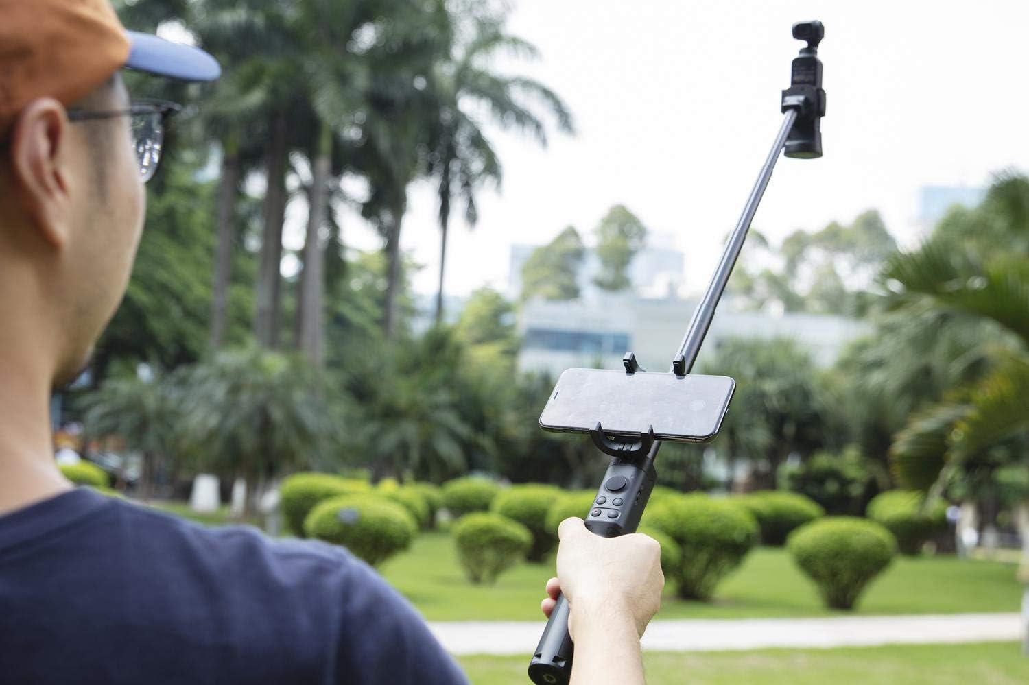 Person holding the DJI Osmo Pocket Extension Rod with camera and phone attached, extended for use.