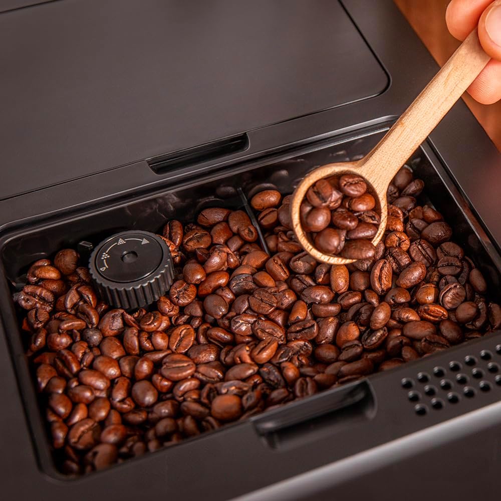 Coffee beans in the machine's grinder with a wooden spoon