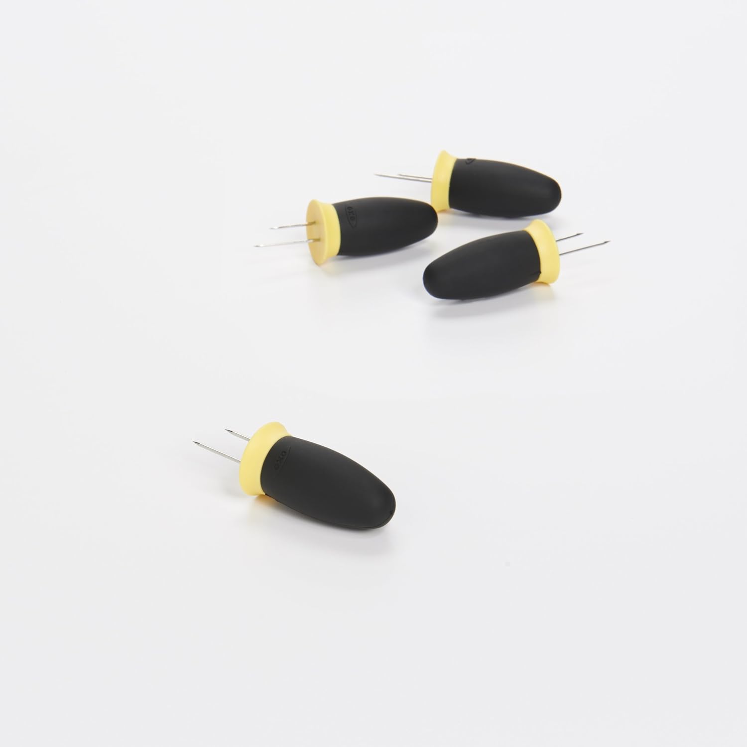 Four OXO Good Grips Corn Holders arranged on a white surface, showing their black handles and yellow collars.
