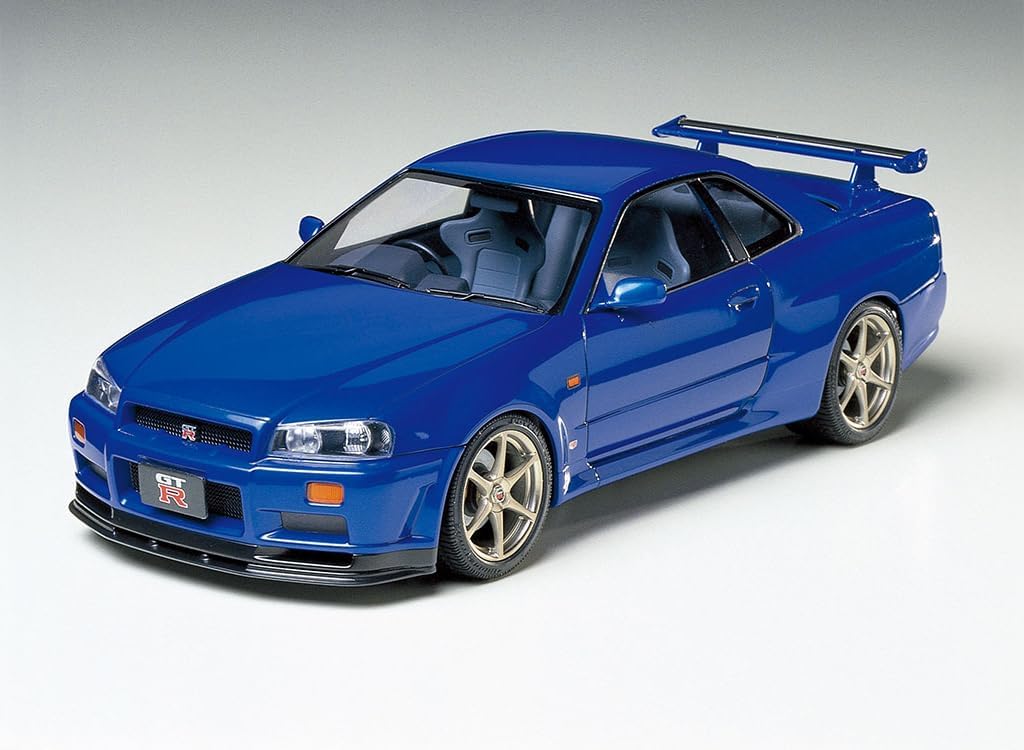 A fully assembled and painted Tamiya Nissan Skyline GT-R R34 model kit in blue, viewed from a slightly elevated rear-left angle.