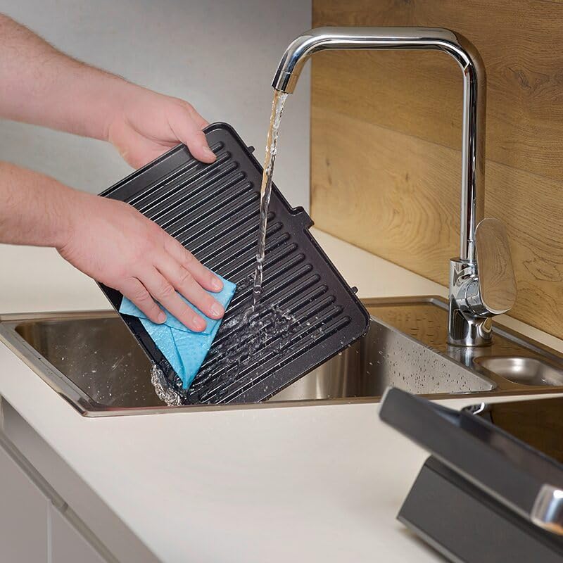 Ruce čistící odnímatelnou grilovací desku pod tekoucí vodou