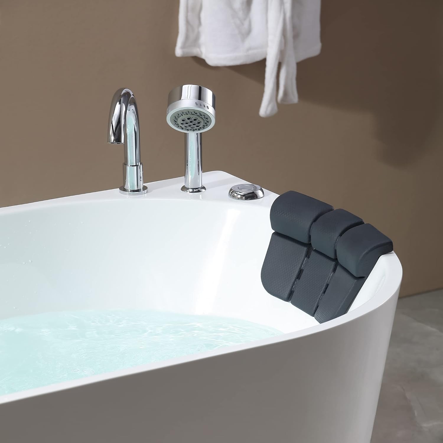 Close-up of bathtub faucet, handheld shower, and black pillow rest