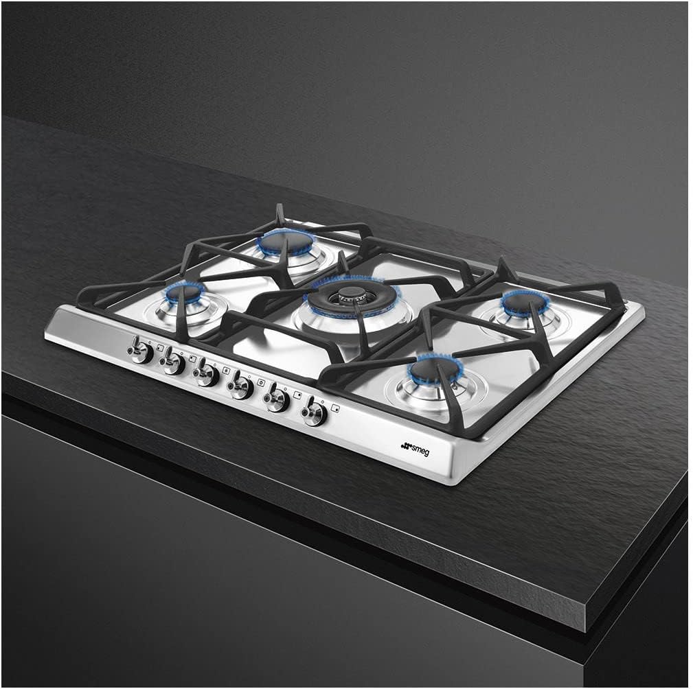 Ugao view of the Smeg SE70SGH-5 gas hob installed in a kitchen countertop, with flames visible on the burners.