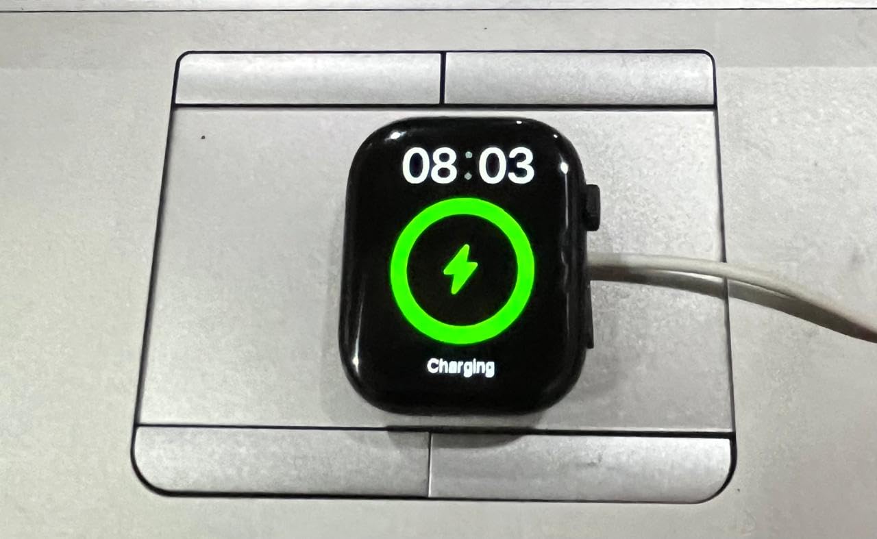 X90 Max Smart Watch displaying '08:03' and a green charging icon with a lightning bolt, indicating it is currently charging. The watch is placed on a white wireless charging puck.