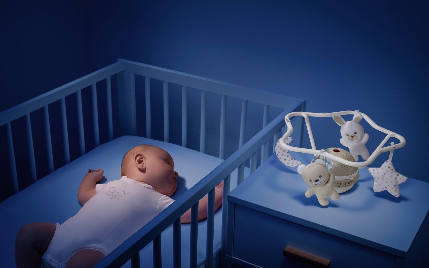 Baby in cot with Chicco mobile unit on bedside table