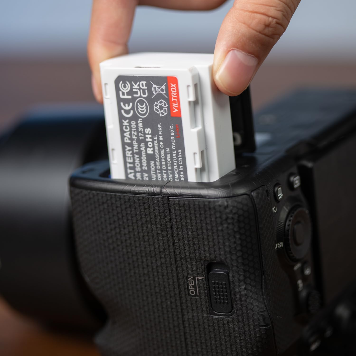 A hand inserting a VILTROX NP-FZ100 battery into a camera battery compartment.