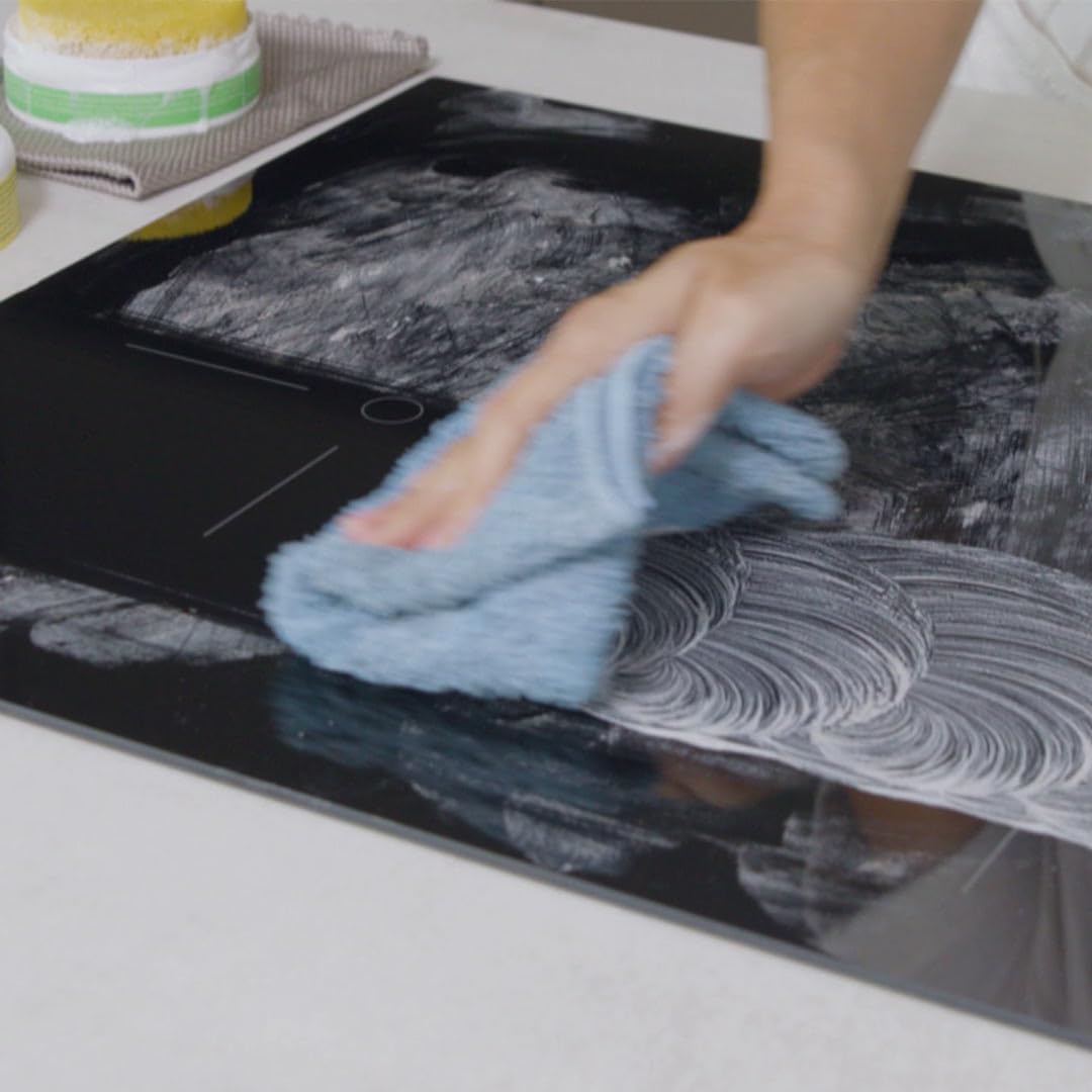 Person cleaning a glass shower door with a yellow sponge and Pure100 MagicShine, creating foam