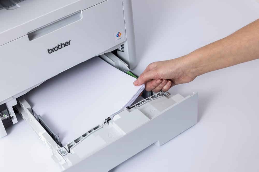 A hand loading a stack of white paper into the paper tray of the Brother MFC-L8390CDW printer.