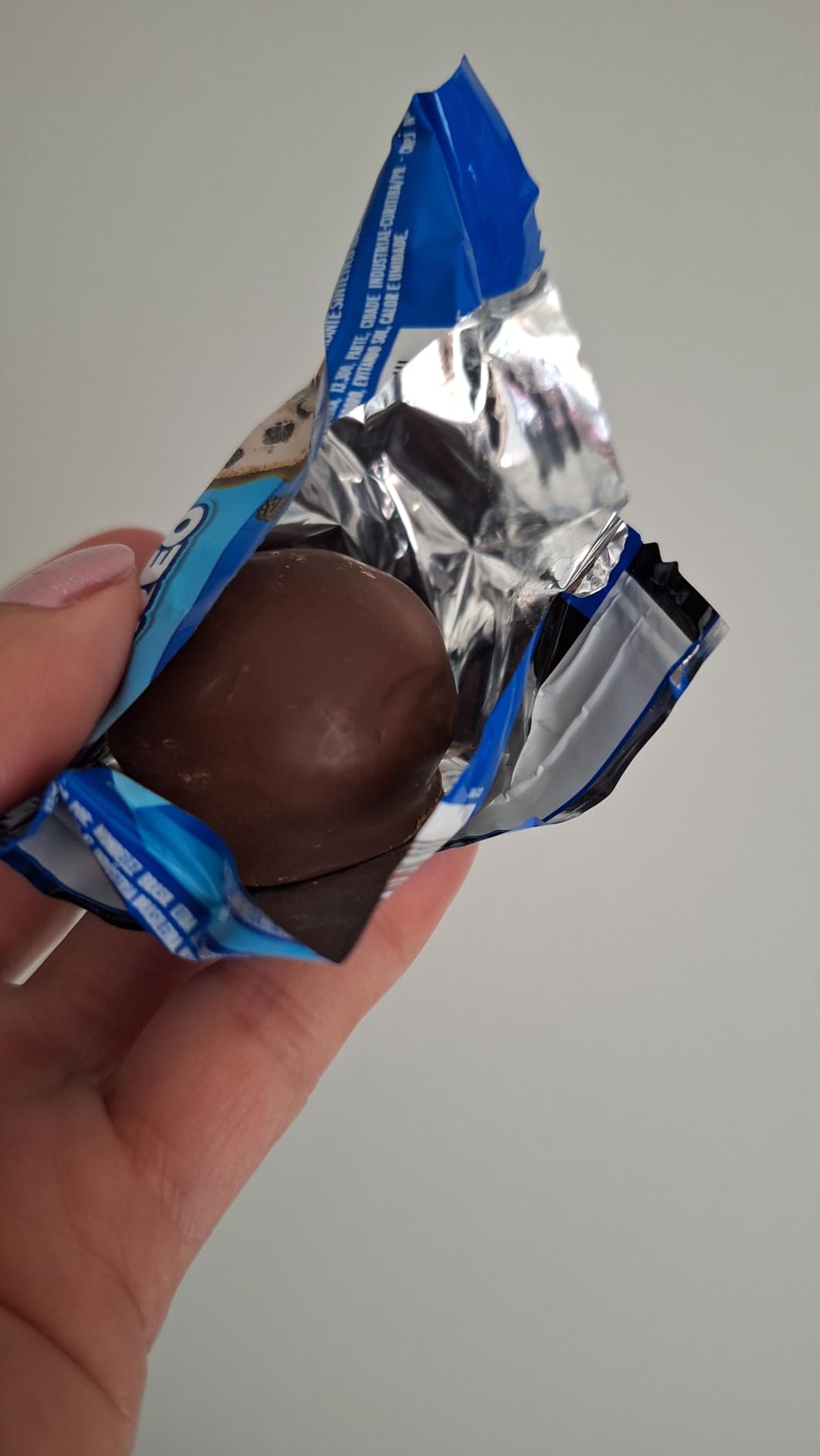 Close em uma mão segurando um bombom Lacta Oreo aberto com a embalagem