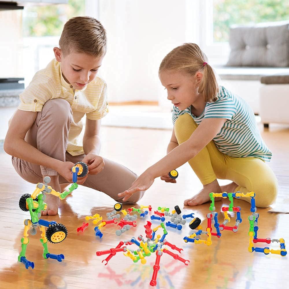 Two children engaged in building with SHUNLAM blocks on a wooden floor, demonstrating collaborative play.