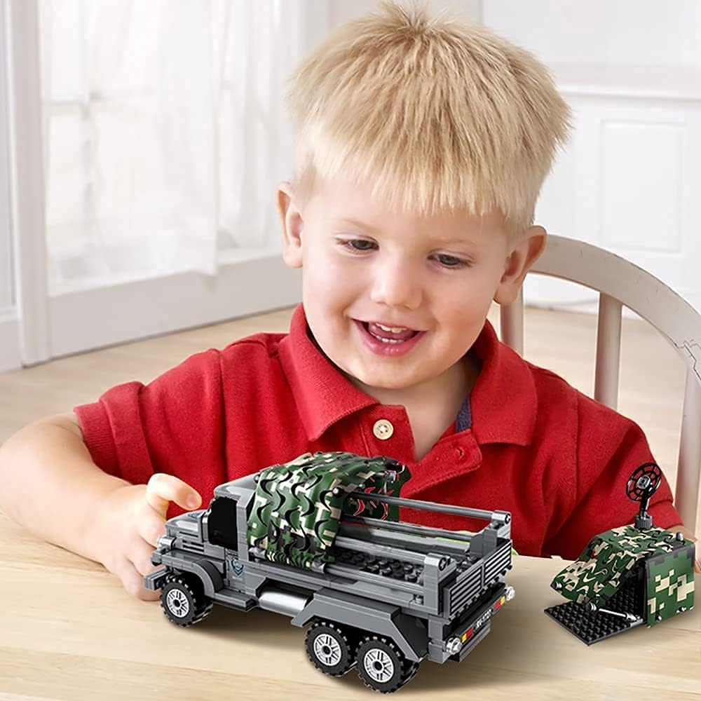 A child happily playing with the assembled QMAN Military Vehicle Building Blocks Set, pushing the truck across a table.