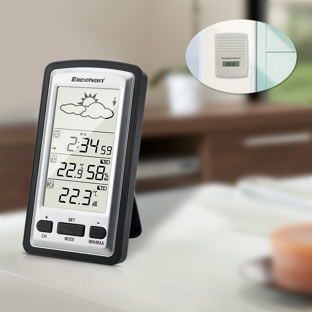 EXCELVAN WH1281 Weather Station main unit on a table with the outdoor sensor visible through a window.