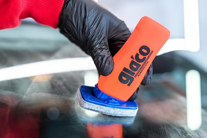 Mão com luva preta segurando o frasco do Glaco DX aplicando o produto em um vidro de carro