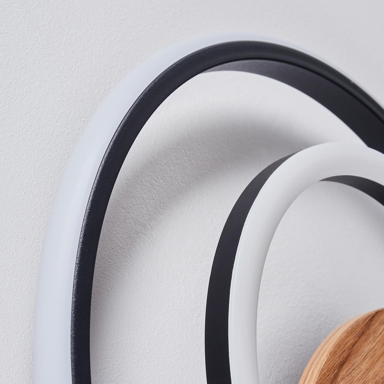 Close-up view of the HOFSTEIN Rapoila LED Wall Light, showing the texture of the wood-look element and the black and white rings.