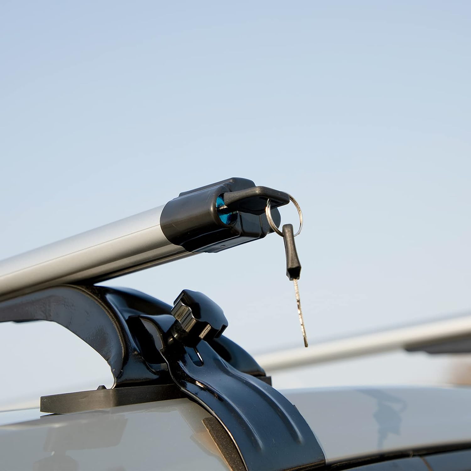 Close-up of the end of a silver roof rack crossbar with a black locking mechanism inserted, showing a key in the lock.