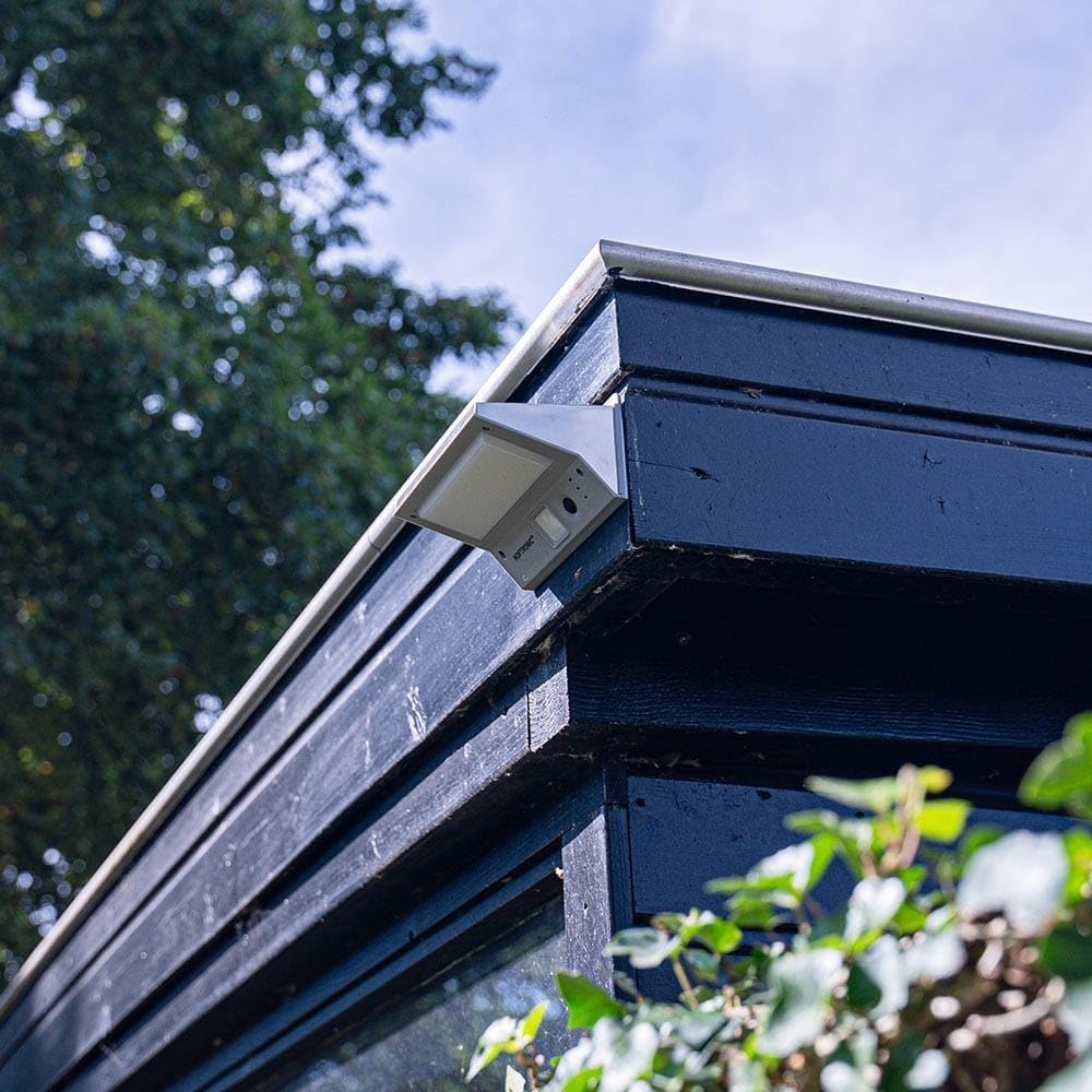 HOFTRONIC Burley Outdoor Solar Wall Light mounted on the corner of a dark wooden shed during daylight.