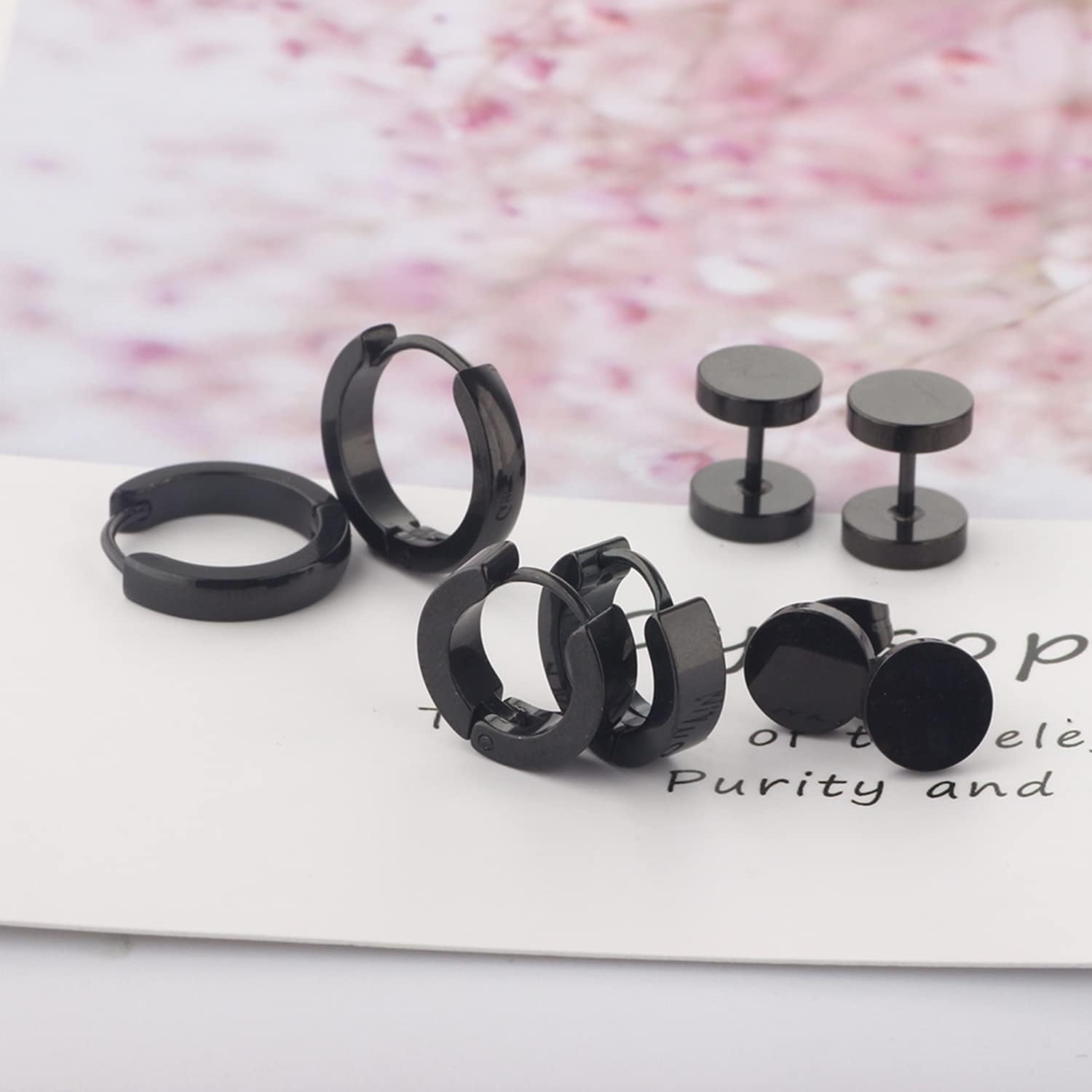 Close-up of various black stainless steel earrings from the set, showcasing different designs like flat discs, hoops, and screw-backs.