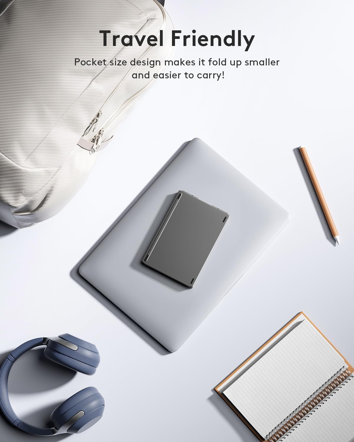 Folded keyboard placed on a laptop next to a backpack and notebook, emphasizing travel-friendliness