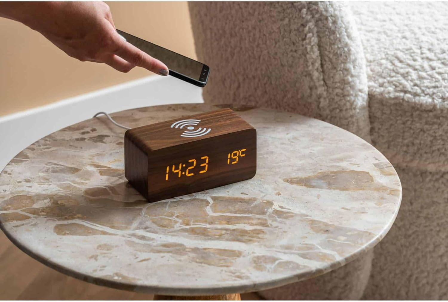 A hand placing a smartphone on top of the Karlsson Alarm Clock for wireless charging.