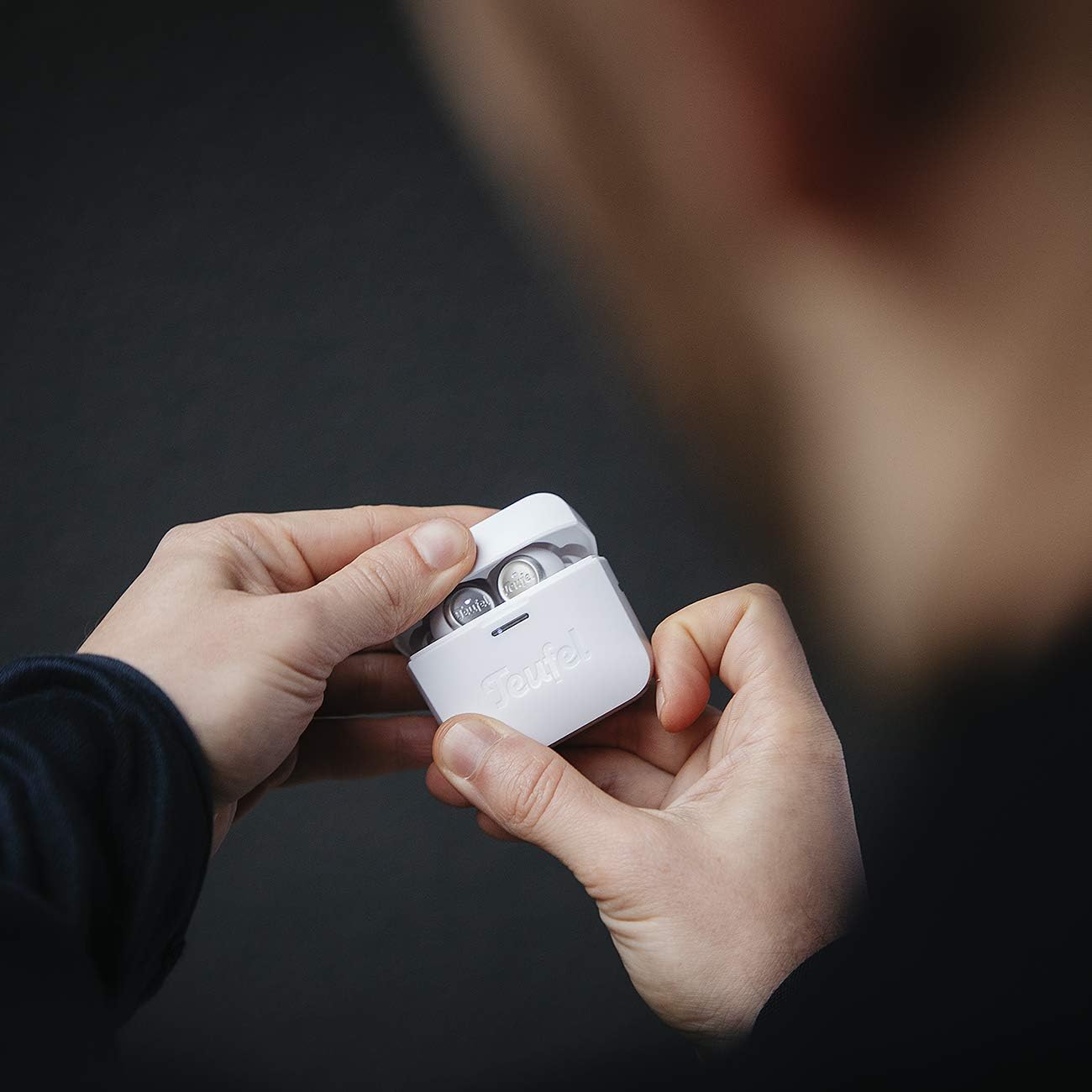 Hands holding the Teufel AIRY TRUE WIRELESS charging case with earbuds inside