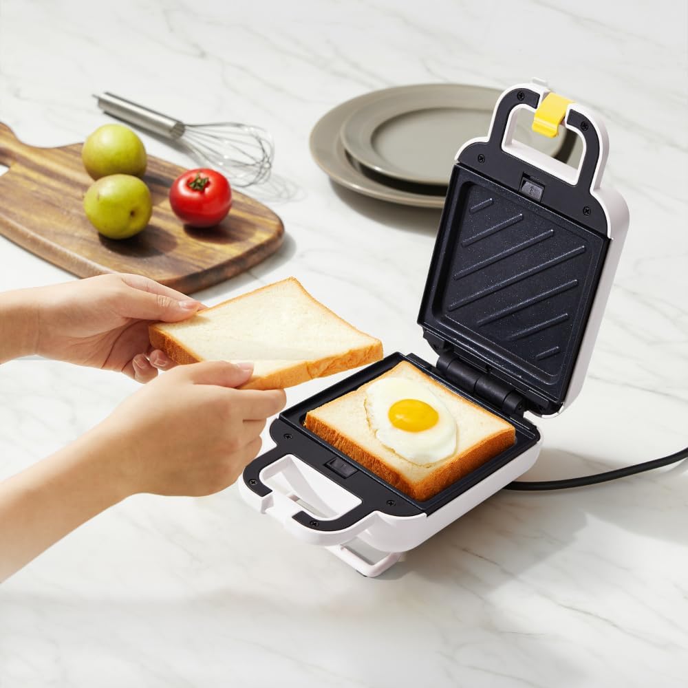 A hand washing a removable grill plate under running water in a kitchen sink.