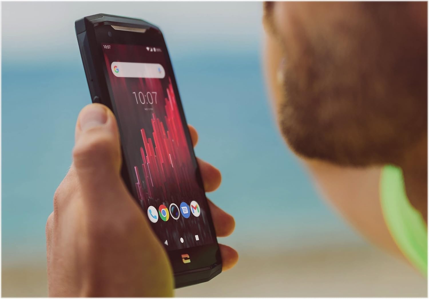 A person holding the Crosscall CORE-M5 smartphone outdoors, showing the display with app icons.