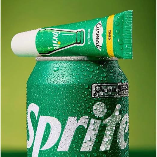 Bisnaga do hidratante labial Carmed Sprite apoiada sobre uma lata de refrigerante Sprite coberta de gotas de condensação