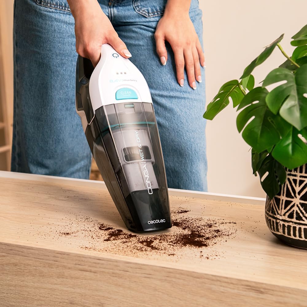 Person vacuuming coffee grounds from a wooden surface with the Cecotec Conga Rockstar