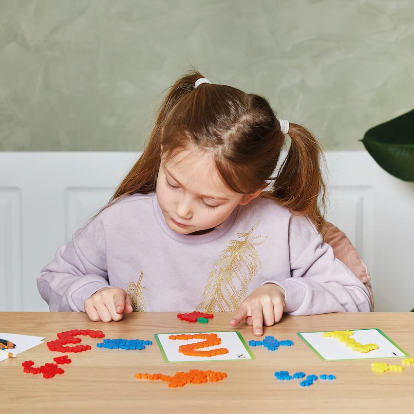 A child focused on building with colorful PLUS PLUS pieces on a wooden table