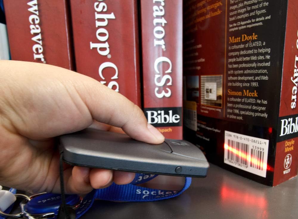 A hand holding the Socket Mobile S840 scanner, aiming its red laser beam at a barcode on a book spine.