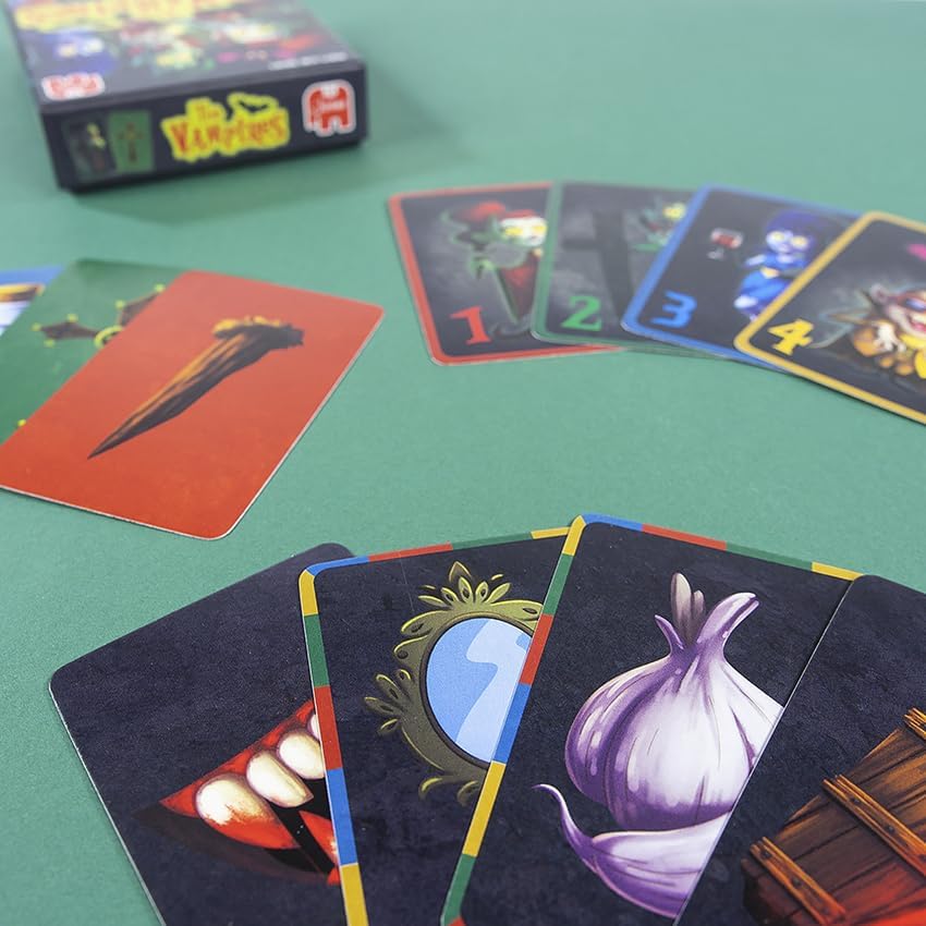 Various game cards laid out on a green surface, showing different types of cards including numbered vampire cards and weapon cards like a wooden stake and garlic.