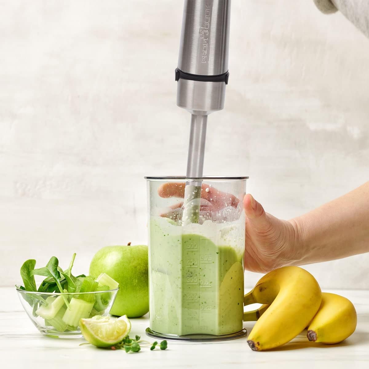 Immersion blender in use, blending a green smoothie in a clear container