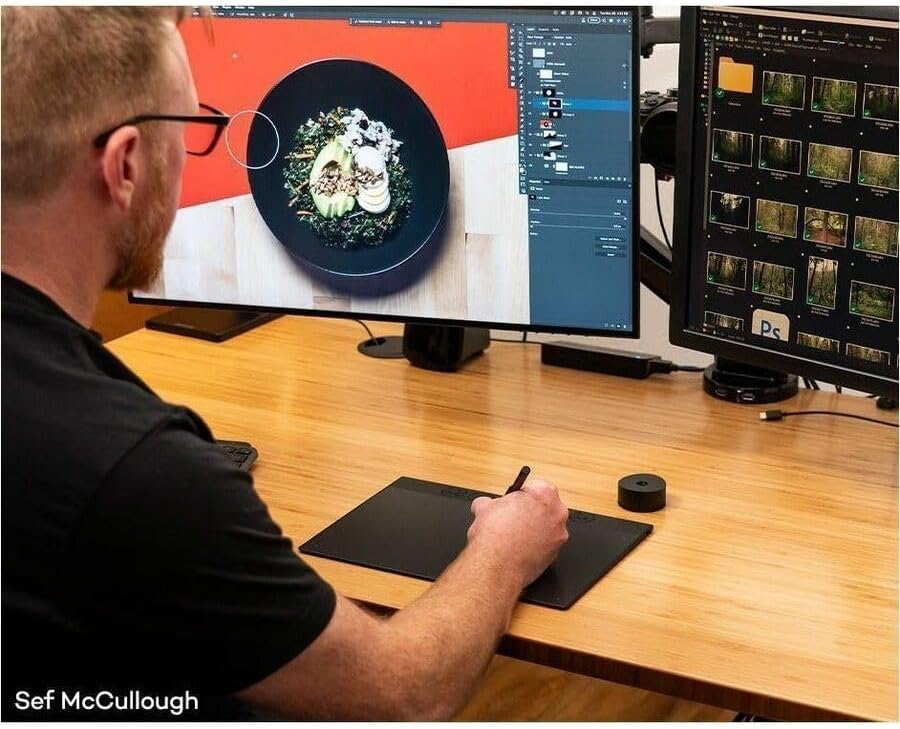 A person using the Wacom Intuos Pro tablet with a pen while working on a computer with dual monitors.