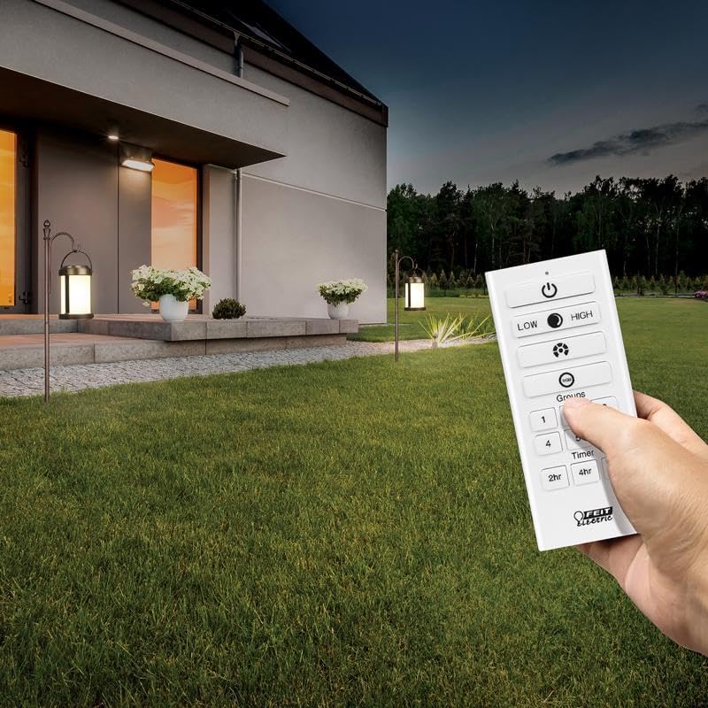 A hand holding a Feit Electric OneSync remote control, with two solar lanterns visible in the background illuminating a house exterior.